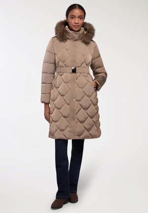 Cappotto imbottito beige con design a rombi, cappuccio con bordo in pelliccia, vita con cintura e chiusura a bottoni. Abbinato a pantaloni blu scuri e stivali marroni.