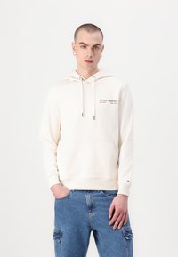 Kremfarget hettegenser laget av myk bomull, med en frontlomme, snorhette og brodert "TOMMY HILFIGER"-logo på brystet.