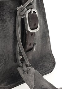 Musta nahkalaukku, jossa on teksturoitu pinta, varustettuna hopeisella metallisoljella ja nahkaremmin kanssa. Koristeina ovat sidottu nahkadata.