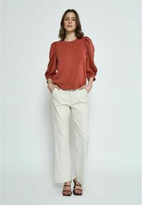 Rustkleurige trui met pofmouwen en een ronde hals, gecombineerd met beige brede broek en zwarte sandalen met bandjes. Eenvoudig en strak ontwerp.