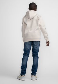 Witte hoodie, denim jeans en grijze sneakers. De hoodie heeft een gladde textuur en een logo op de linker mouw.