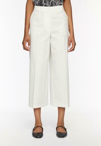 Pantaloni a gamba larga in tessuto crema chiaro, caratterizzati da un'alta vita e una texture liscia. Abbinati a ballerine nere per un look completo.