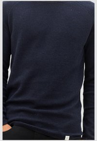 Marineblauwe gebreide trui met een gestructureerd oppervlak, lange mouwen en een ronde halslijn, voorzien van een klein label aan de zoom.