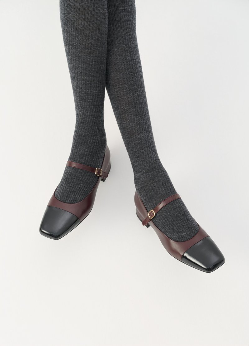 Mary Jane-skor i bordeauxläder med svart lacktå, liten klack och spännsnodd. Pairad med mörkgrå ribbade strumpor.