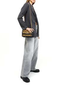Svart och beige leopardmönstrad axelväska med ett guldkedjesnöre, har en klaffstängning och svarta detaljer. Bärs tillsammans med grå vida jeans.