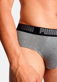 Graue Baumwoll-Unterhosen mit einem schwarzen Bund, der den erhabenen "PUMA"-Schriftzug zeigt. Nahaufnahme, die die Stoffbeschaffenheit und Passform hervorhebt.