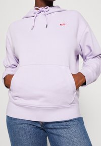 Felpa viola chiaro realizzata in tessuto morbido, con tasca frontale, cappuccio regolabile con cordino e un piccolo logo rosso Levi's.