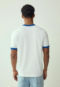 T-shirt bianco con colletto e orli delle maniche blu a coste, maniche corte e vestibilità comoda, abbinato a jeans azzurri.