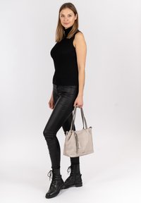 Haut sans manches en maille noire, leggings noirs brillants, bottes noires à lacets et sac à main texturé gris clair avec des accents de pompons.