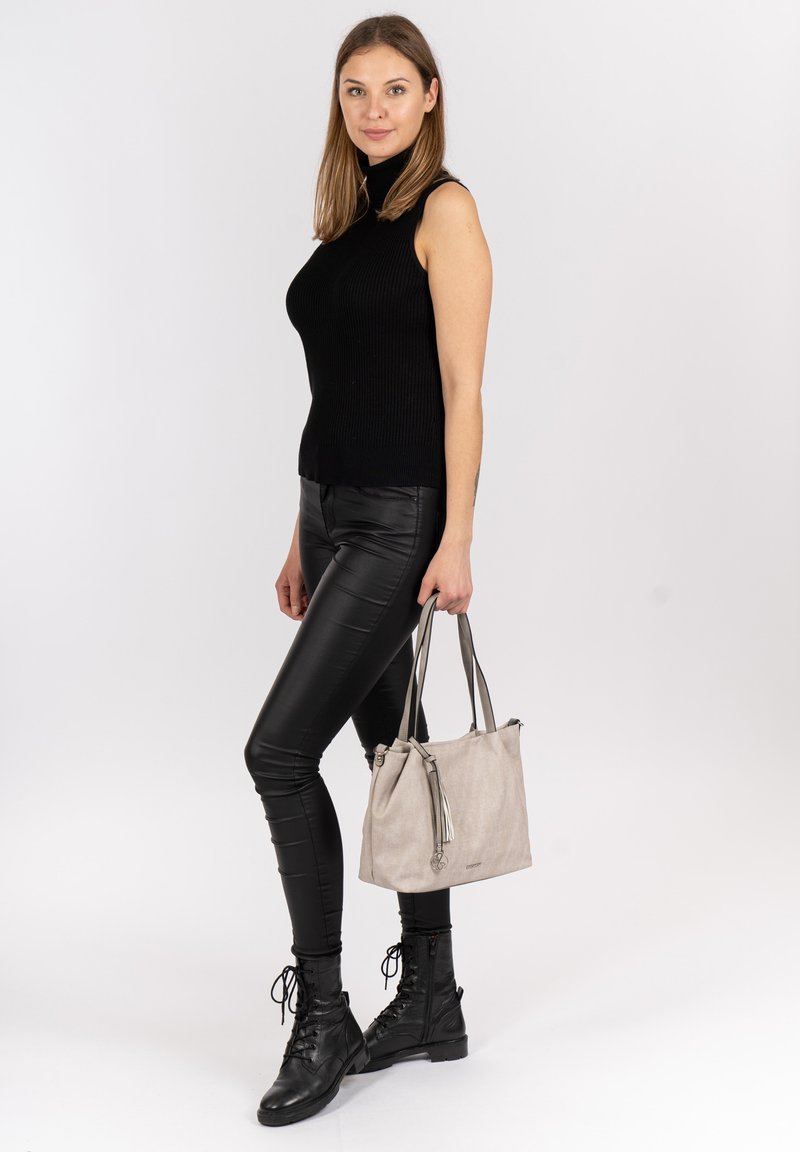 Haut sans manches en maille noire, leggings noirs brillants, bottes noires à lacets et sac à main texturé gris clair avec des accents de pompons.