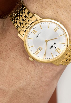 Gouden polshorloge met een witte wijzerplaat, Romeinse cijfers, een datumaanduiding die de 31e toont, en een gouden schakelband om de pols van een persoon.