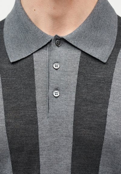 Εγγύς πλάνο ενός ατόμου που φορά γκρι πόλο πουκάμισο με σκούρες και ανοιχτές κάθετες ρίγες και τρία μαύρα κουμπιά κουμπωμένα στον γιακά.