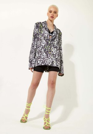 Blazer with bold black and white graphic print and neon green accents, paired with black biker shorts and neon strappy heels.