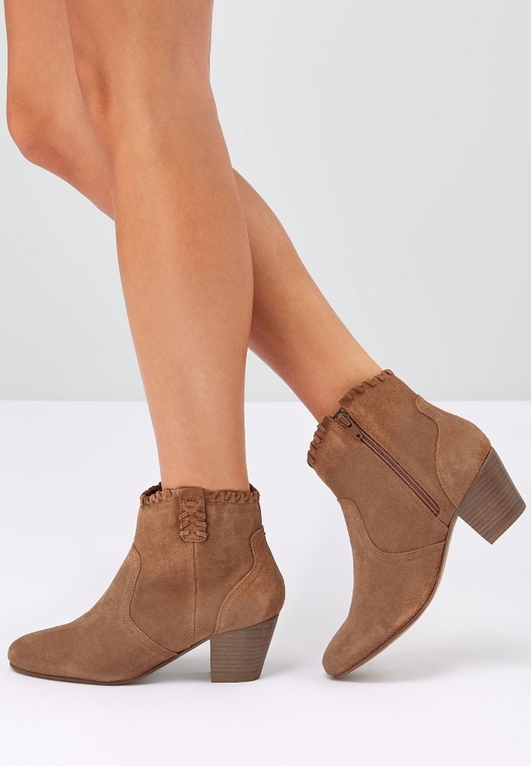 Brown suede ankle boots with a short stacked heel. Features a ruffled edge at the top and a side zipper for easy wear.