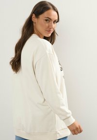 Felpa oversize color crema con scollo tondo, spalle cadenti e grafica a stampa leopardo. Texture morbida, polsini e orlo a coste.