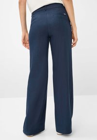 Pantaloni a gamba larga navy con una texture liscia, dotati di vita a media altezza e due tasche posteriori. Dettaglio del logo discreto sulla cintura.