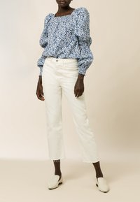 Blå blomstret bluse med puffede ærmer og firkantet halsudskæring; kombineret med hvide cropped jeans og beige slip-on sko. Glat tekstur.