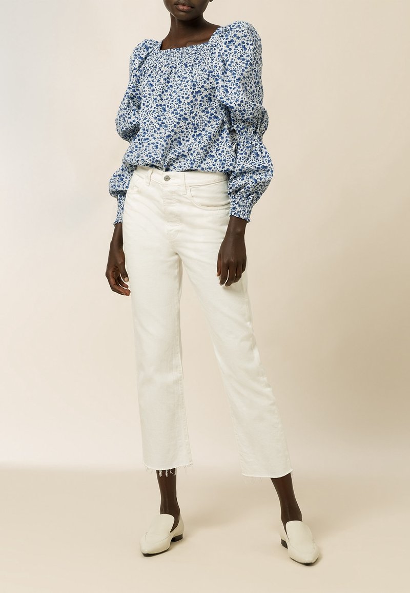 Blå blomstret bluse med puffede ærmer og firkantet halsudskæring; kombineret med hvide cropped jeans og beige slip-on sko. Glat tekstur.