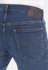 Mellanhöga blå denimjeans med en brun läder etikett i midjan. Kontraststickning, klassisk femficksdesign och lätt blekning.