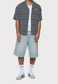 Kortärmad svart och vit mönstrad skjorta, vit tanktop, ljusa denimshorts, blå sportskor med vita sulor och vita strumpor.