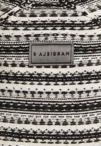 Tissu tissé rayé noir et blanc avec une étiquette rectangulaire grise cousue au centre avec un texte inversé.