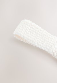 Biely pletený čelenok s textúrovaným rebrovaným vzorom. Jemný, elastický materiál s hladkým povrchom. Vhodný na bežné nosenie.