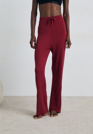 Red relaxed-fit pants made of soft fabric with a drawstring waist, featuring a flared design and a smooth texture, worn barefoot.