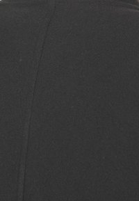 Indumento nero con una superficie testurizzata, caratterizzato da una cucitura visibile che corre verticalmente lungo la schiena. Materiale morbido e caldo.