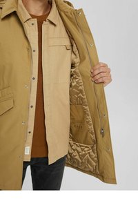 Kurtka khaki na zamek błyskawiczny z kieszeniami na zatrzaski i pikowaną podszewką wewnętrzną. Posiada gładką zewnętrzną powierzchnię i teksturowaną tkaninę wewnętrzną.