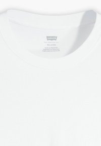 Biała bawełniana koszulka z luźnym krojem, okrągłym dekoltem oraz metką z nazwą marki, krajem produkcji i instrukcjami prania.