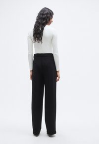 Μαύρο παντελόνι με φαρδύ πόδι, λεία υφή και ψηλή μέση, συνδυασμένο με εφαρμοστό λευκό τοπ μακρυμάνικο. Απλός, μινιμαλιστικός σχεδιασμός.