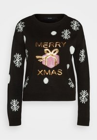 Svart stickad tröja med vita snöflingor och polka prickar. Guldpaljetterat text "GOD JUL" och en rosa presentlåda design i mitten.