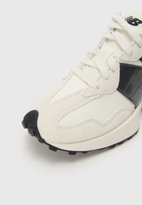 Gros plan sur une chaussure New Balance blanche et noire montrant les textures en suède, les lacets et la semelle en caoutchouc crantée.