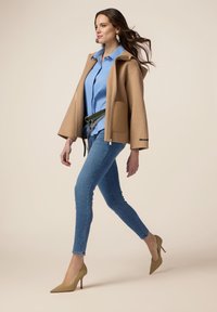 Abrigo de mezcla de lana en tono marrón claro con frente abierto, camisa abotonada en azul claro, jeans skinny de denim y zapatos de tacón nude. Textura suave y líneas limpias.