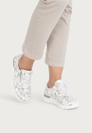 Legs wearing beige cropped pants and white lace-up sneakers with gray snakeskin pattern and thick white soles, one foot slightly raised.