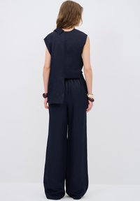 Mörkblå byxdress med vida ben och ärmlös överdel, med en bakre luckdetalj och elastisk midja, tillverkad av ett lätt material.