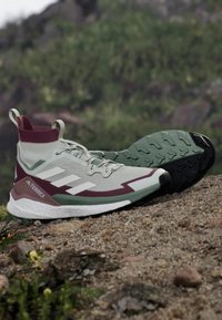 Vaaleanvihreä vaelluskengä, jossa on maroonit yksityiskohdat, teksturoitu päällinen, valkoinen pohja ja erottuva urakuvio, joka tarjoaa pitoa. Varusteena on tukeva nilkkakotelo.