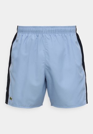 Lyseblå badeshorts med svart sidepanel, elastisk midje og hvit piping. Har en liten grønn logo ved kanten.
