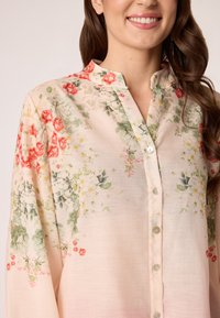 Bloemige overhemden met knopen van lichte roze stof, groene en rode bloemenprints, en een kraag met een pat voor doorschijnende knopen.