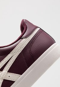 Sneaker in pelle bordeaux con superficie testurizzata, suola bianca e accenti bianchi a contrasto lungo il lato. Design con punta rotonda.