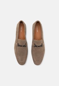 Brown suede loafers with a textured finish, featuring a black metal accent across the front and a beige leather insole.