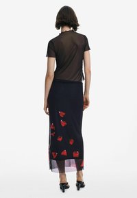 Schwarzes Mesh-T-Shirt mit kurzen Ärmeln, übereinander getragen mit einem langen navyblauen Rock, der mit roten Blütenblättern bedruckt ist und einem durchsichtigen Saum.