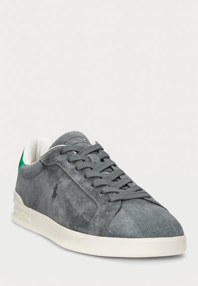 Grijze suède sneaker met groene hielaccent, vetersluiting ontwerp en een contrasterende witte zool. Heeft een klein logo aan de zijkant.