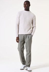 Suéter de punto acanalado beige claro con cuello redondo, combinado con pantalones gris claro y zapatillas blancas con detalles en negro.