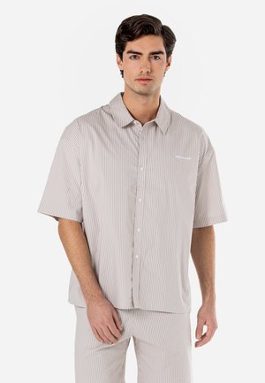 Camicia corta a maniche corte a righe color beige chiaro con righe più scure a contrasto. Presenta un colletto e bottoni frontali.
