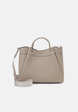 Sac à main beige texturé avec deux poignées et une sangle détachable portant le texte "Exchange", sur un fond blanc uni.