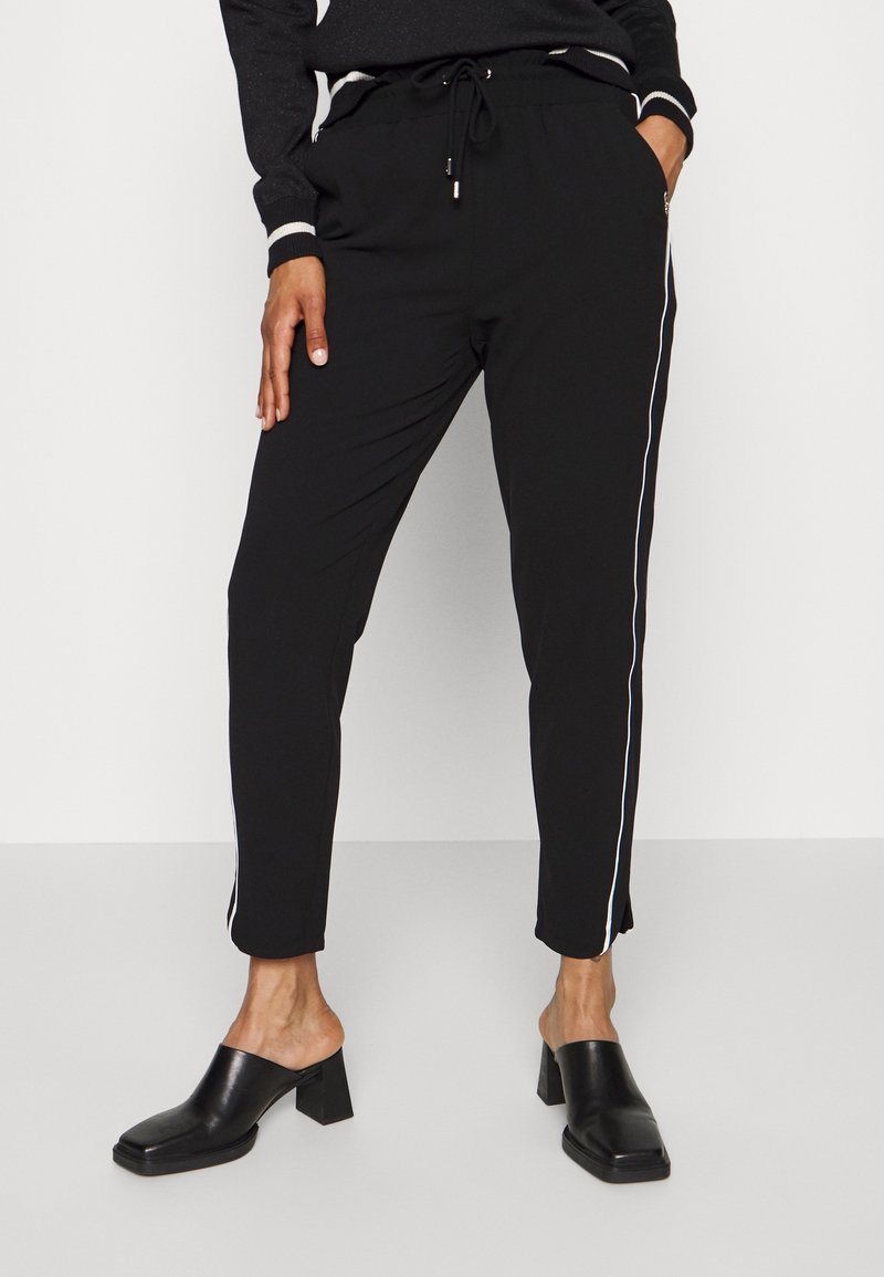 Pantalon de jogging noir avec des bandes latérales blanches, en tissu doux. Dispose d'une taille à cordon de serrage et de jambes fuselées, associé à des mules à talons blocs à bout ouvert.