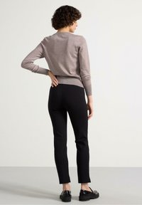 Maglioncino grigio a maglia con maniche lunghe, abbinato a pantaloni neri aderenti e calzature nere. Il maglione ha un collo arrotondato e un orlo a coste.