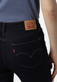 Jeans azul oscuro con un corte slim, que presentan costuras doradas, un parche de cuero en la parte posterior, y un diseño de bolsillo curvado distintivo.