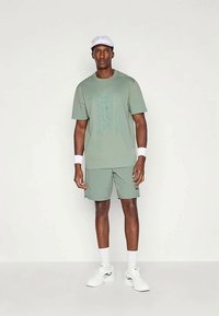 Lys grønn treningstøy bestående av t-skjorte og shorts, med en stor logo, kombinert med hvite tilbehør og sko.